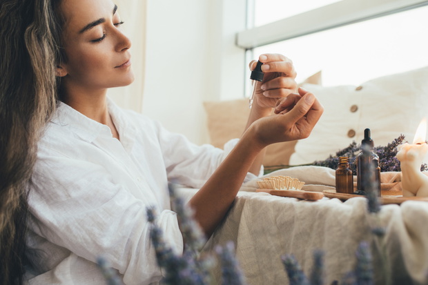 Young woman applying natural organic essential oil on hair and s