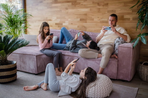Family with two little daughters, everyone is using mobile phone in the living room.