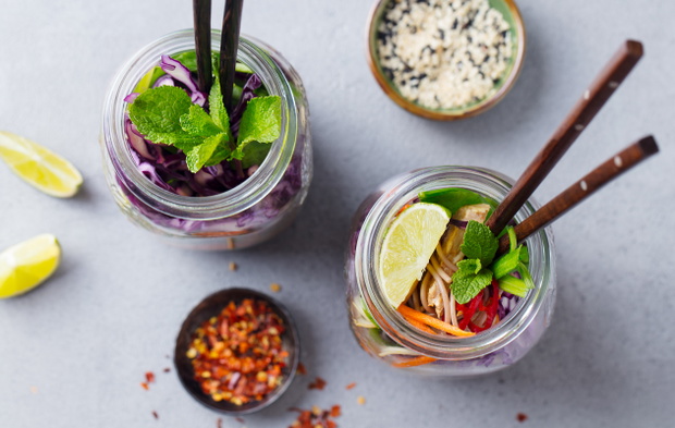 Noodles soba salad, soup with vegetables, tofu and chicken in jars. Grey background. Top view.