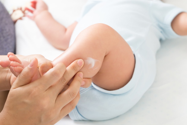 Mother is applying cream to the baby boy which helps to maintain skin leg hydration, Skincare and moisturizing cream concept