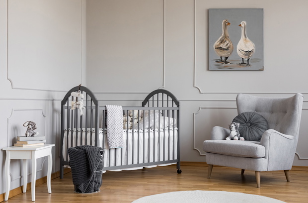 Stylish grey baby room with wooden crib, comfortable armchair an