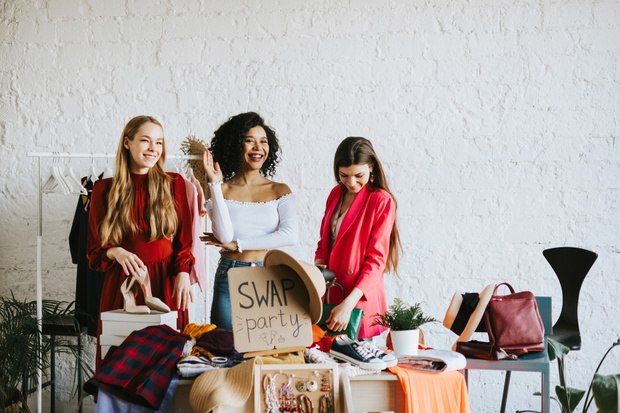 three young woman female caucasian and african students at swap party try on clothes, bags, shoes and accessories, change clothes with each other, second hand for things, zero waste life, eco-friendly