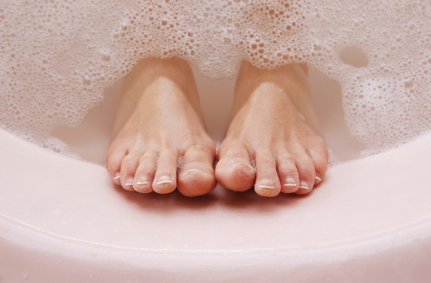 woman's feet resting against bath tub with bubbles