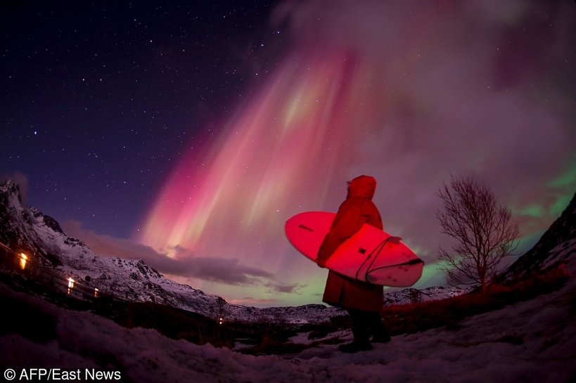 A surfer looks at the Northern lights ( aurora borealis ) illuminating the sky over the snow covered beach of Unstad, on Lofoten Islands, Arctic Circle, on March 14, 2016.