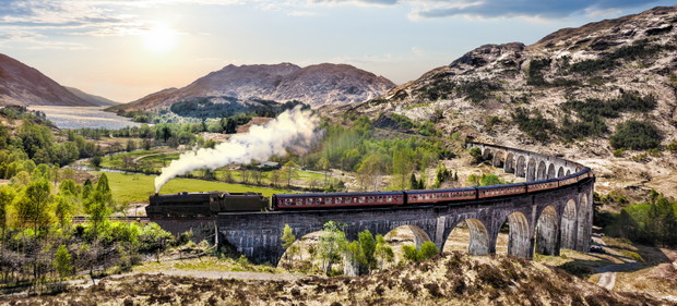 Glenfinnan Railway Viaduct in Scotland with the Jacobite steam train against sunset over lake