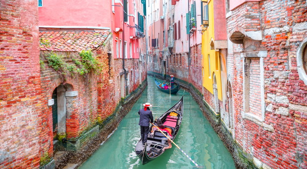 Venetian gondolier punting gondola through green canal waters of Venice Italy