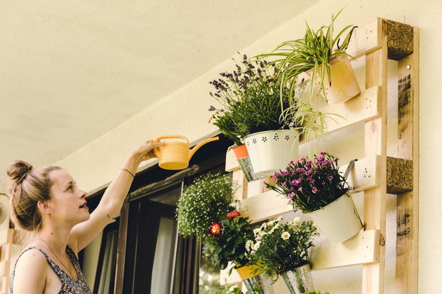 beautiful young woman watering her potted plants on the balcony