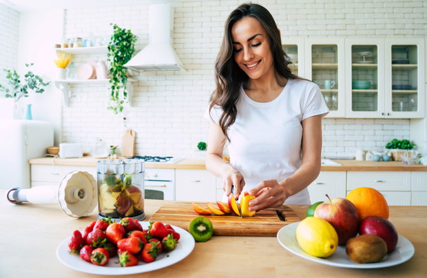 Beautiful woman making fruits smoothies with blender. Healthy eating lifestyle concept portrait of beautiful young woman preparing drink with bananas, strawberry and kiwi at home in kitchen.