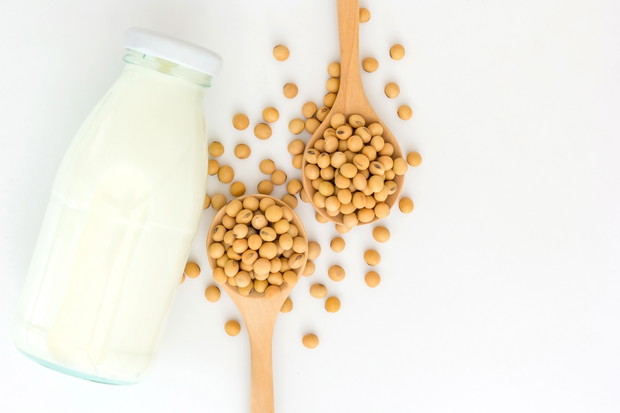 soy milk in glass bottle with soy beans in spoon on wooden background, Top view with copy space and text.