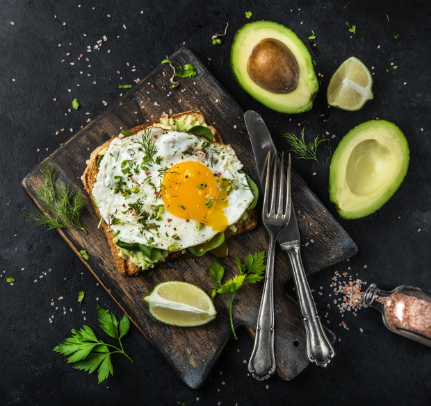 toast with avocado, spinach and fried egg on wooden cutting board, black background