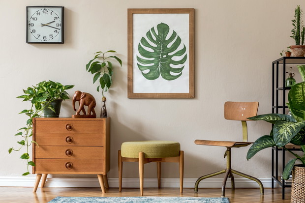 Vintage interior design of living room with design retro furnitures, plants, shelf, black clock and brown poster mock up frame on the beige wall. Stylish home decor. Template.
