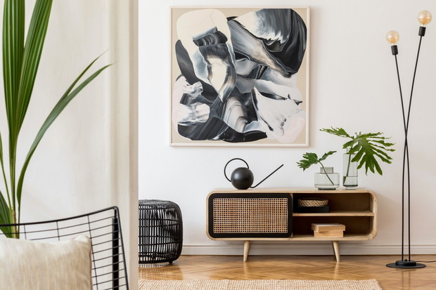 Scandinavian and design home interior of living room with wooden commode, design black lamp, rattan basket, plants and elegant accessories. Stylish home decor. Template. Mock up poster paintings.