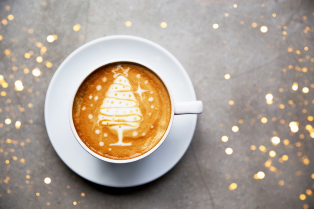 Tasty cappuccino with Christmas tree latte art with some blurred lights.