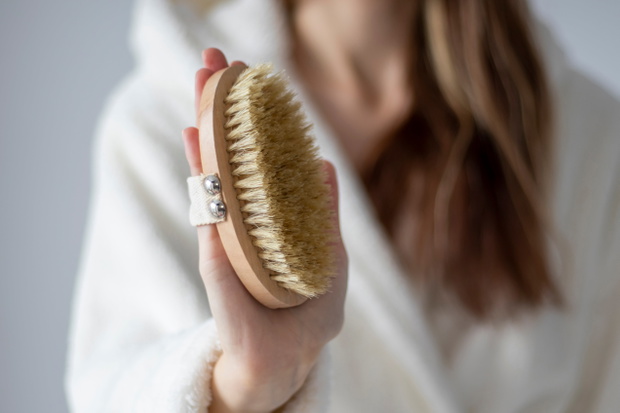 Body brush for dry massage in women's hands. Brushing body to reduce cellulite, detoxify the lymphatic system, and achieve beautiful smooth skin. Body treatment after shower