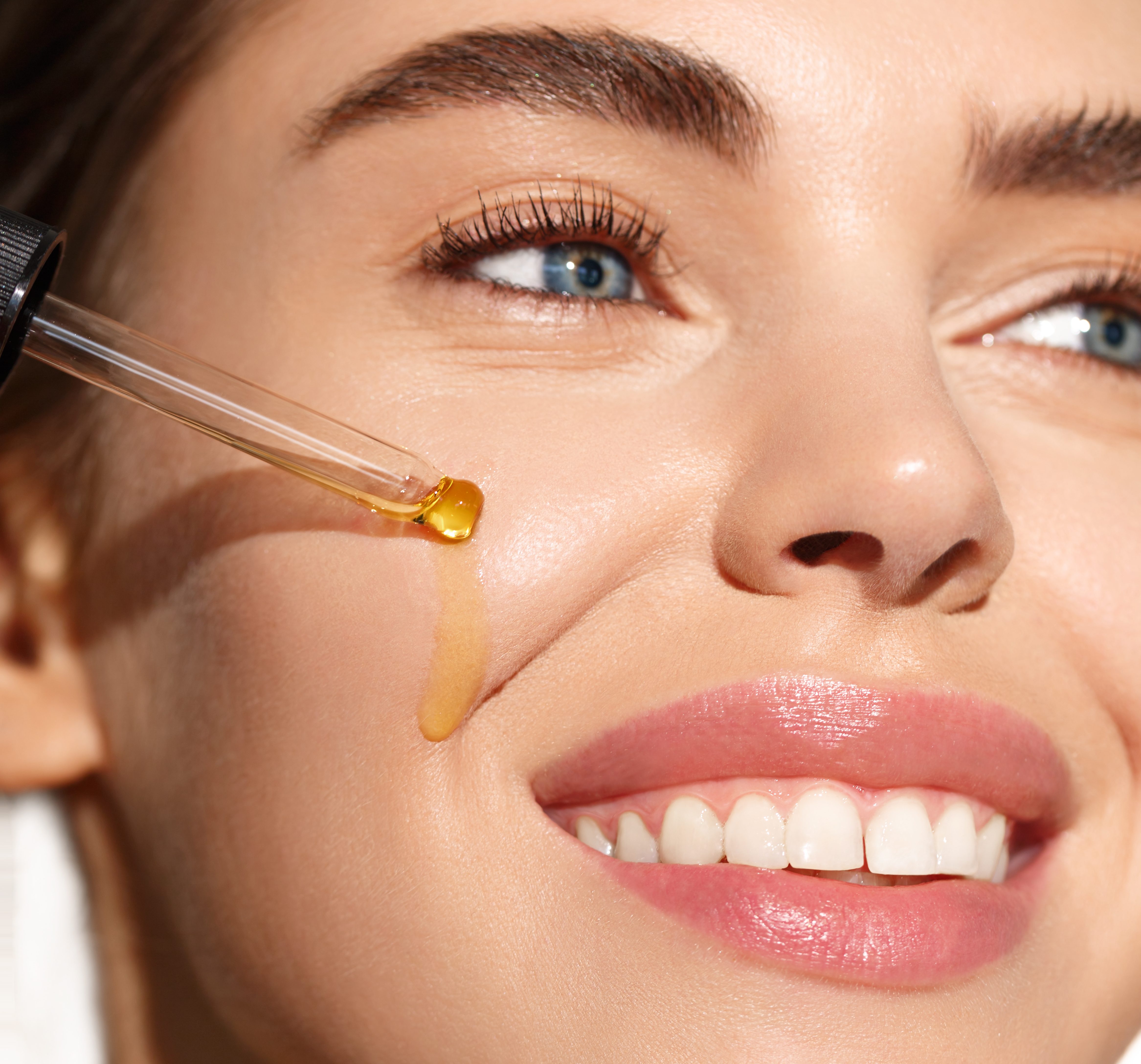 Skin care. Young woman apply moisturizing facial serum, hand holding dropper with essential oil, isolated on white background. Skincare and rejuvenation concept