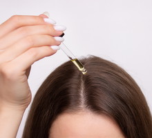 A young woman applies a drop of oil from a pipette to her scalp, close-up. Vitamins, keratin for treatment, strengthening and growth of hair. Problems with dandruff, hair loss. Hair care concept