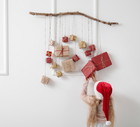 Cute little girl in Santa hat and Christmas advent calendar hanging on light wall