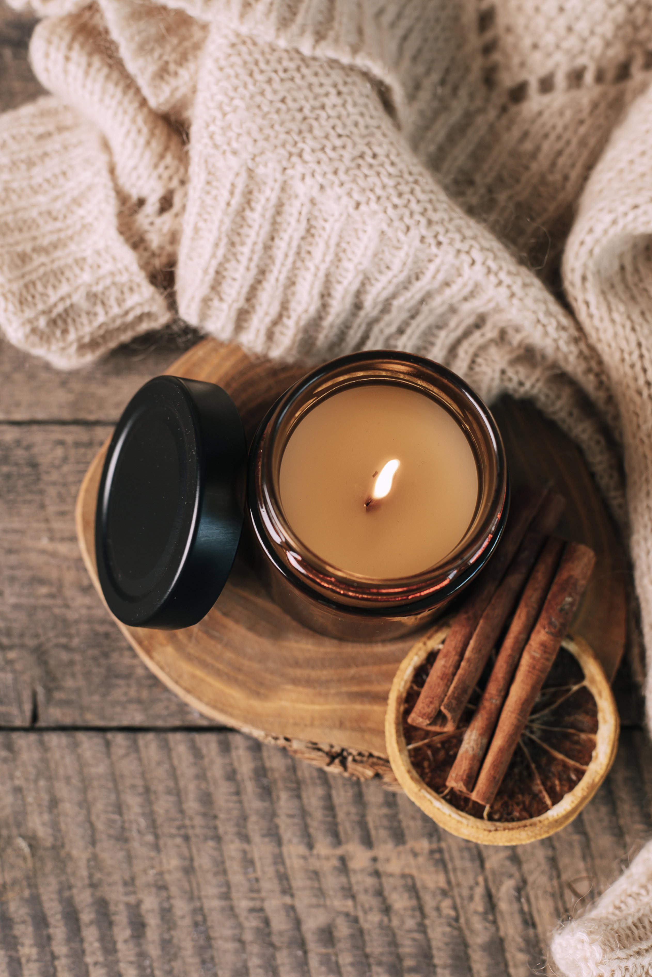 Candle in small amber glass jar with wooden wick on wooden stand on background. Top view