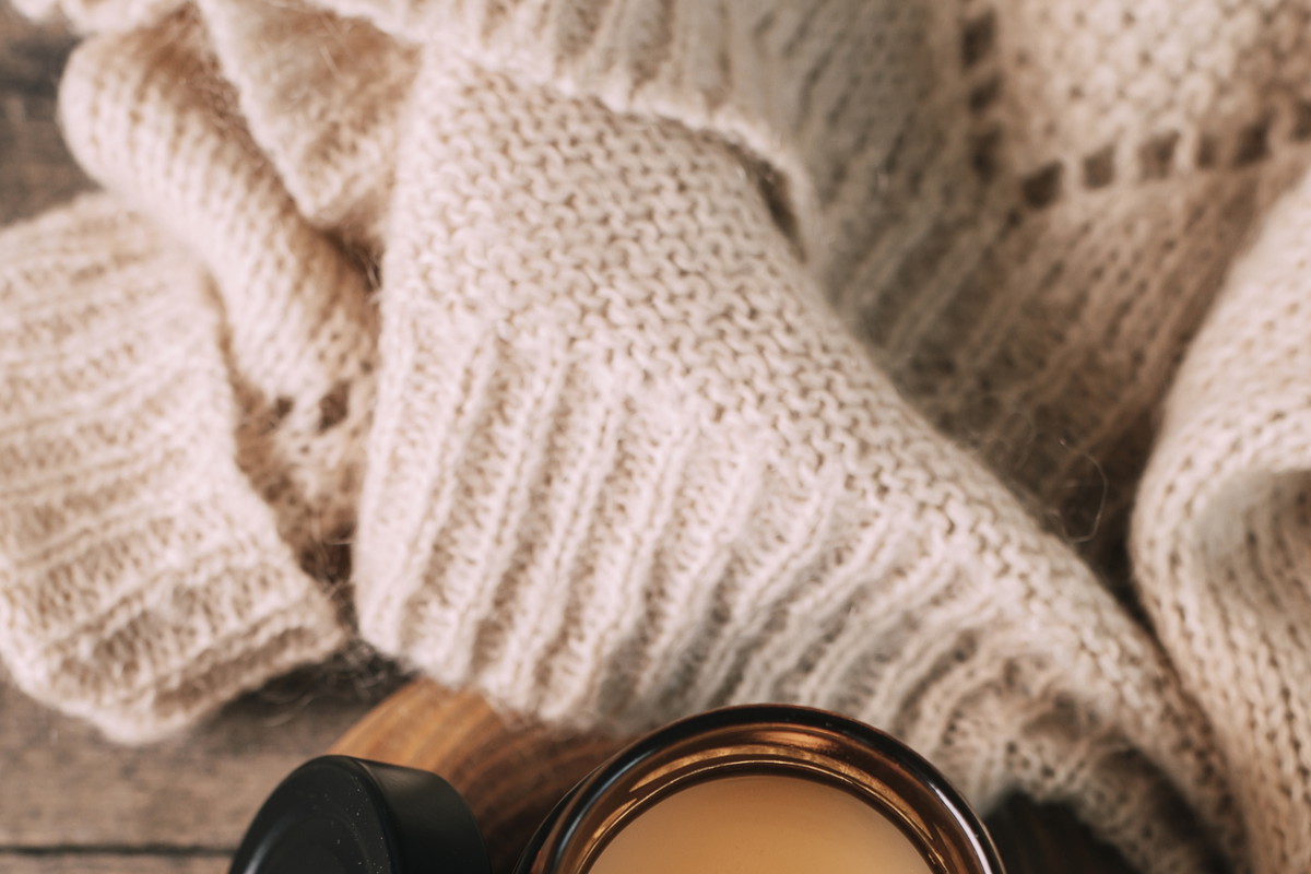 Candle in small amber glass jar with wooden wick on wooden stand on background. Top view