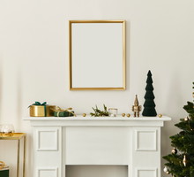 Christmas composition with gold mock up poster frame, white chimney and decoration. Christmas trees and wreath, candles, stars, light and elegant accessories. Template.