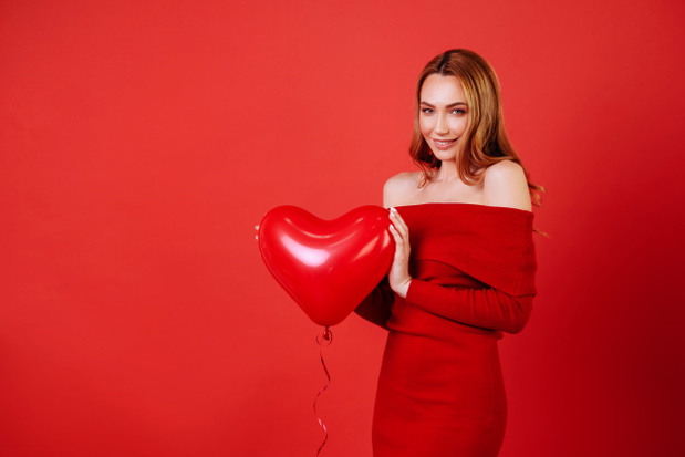 Young charming girl with long curly hair, in red dress holding air balloons, posing at camera.