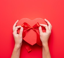 Close up on female hands holding a gift in a pink heart presents for valentine day, birthday, mother's day. Flat lay. Symbol of love. Valentines day background with a gift boxes on concrete board.