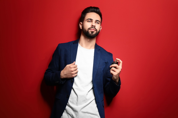 Handsome man with bottle of perfume on color background