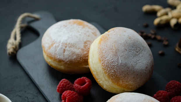 Pączki z cukrem pudrem. Maliny, orzechy, kawa. Ciemne tło, widok z góry.