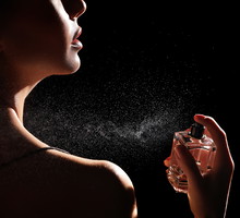 Woman spraying luxury perfume on black background, closeup
