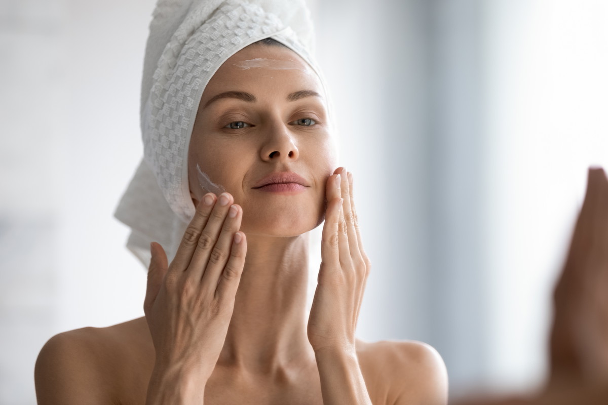 Smiling young pretty lady wrapped in towel smoothing perfecting skin.
