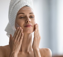 Smiling young pretty lady wrapped in towel smoothing perfecting skin.