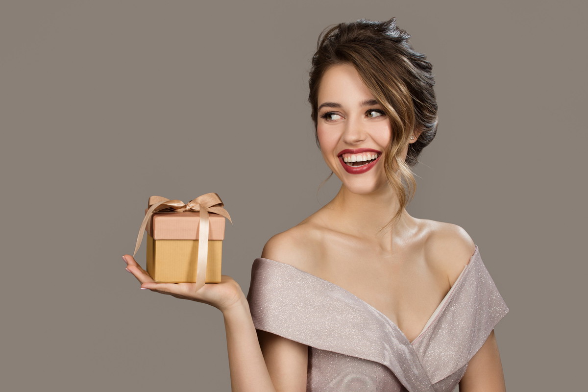 Portrait of smiling pretty woman holding a gift box in hands. Gray background.