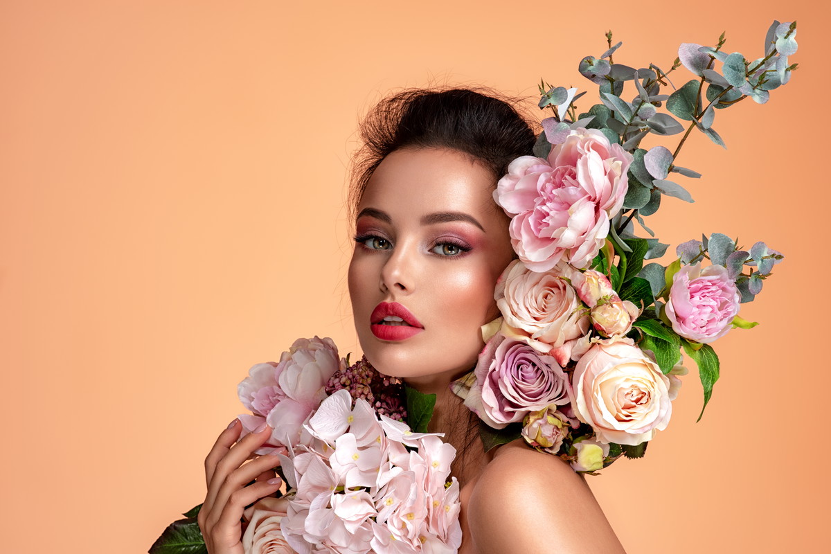 Attractive brunette girl with big beautiful bouquet of flowers. Beautiful white girl with flowers. Pretty woman with bright makeup. Art portrait with flowers.