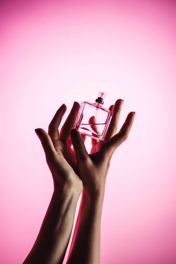 cropped view of woman holding perfume bottle, isolated on pink