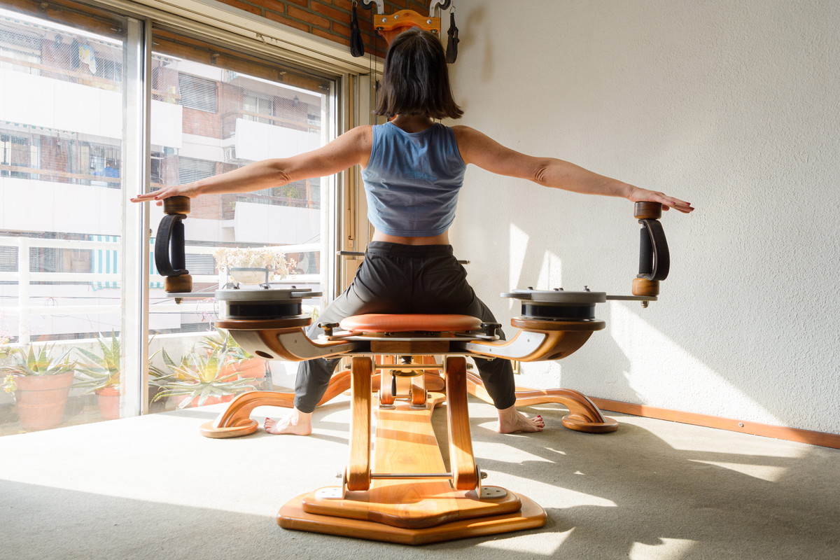 back view of woman working out and stretching shoulder joints on fitness machine at home