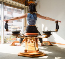 back view of woman working out and stretching shoulder joints on fitness machine at home