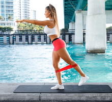 Fitness woman doing kickback exercise for glute with resistance band, outdoors. Athletic girl workout