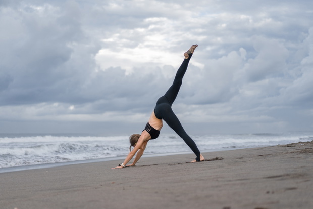 sporty young woman practicing yoga in One Legged Downward-Facing Dog pose (Eka Pada Adho Mukha Svanasana) on seashore