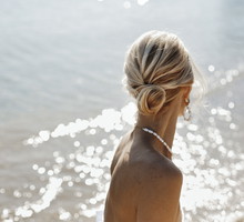 Back view of blonde hairdo and necklace on the naked shoulders near the sea on the sunny summer day