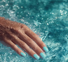 Sparkly turquoise nail polish on wet hand in shimmering blue water
