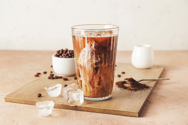 Wooden board with glass of cold brew and coffee beans on beige table