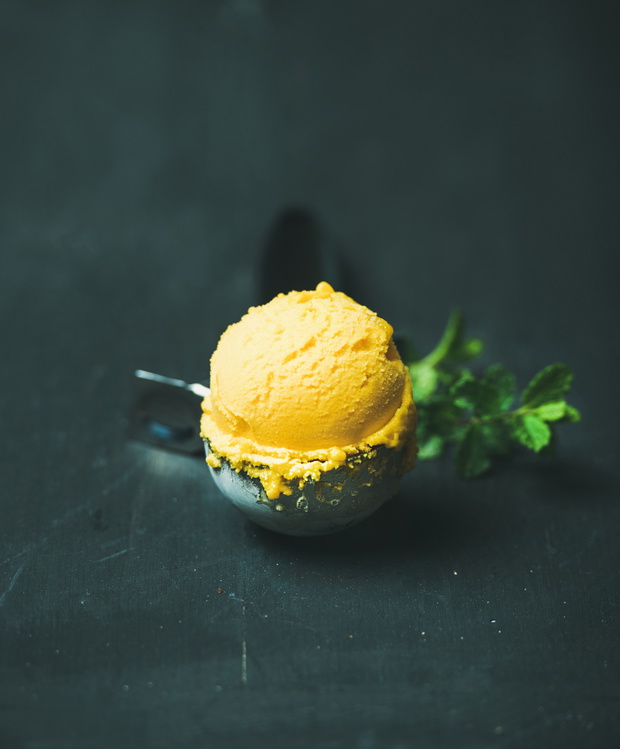 Mango sorbet ice cream scoop in scooper over wooden background