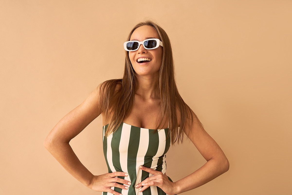 A stylish tanned woman on a beige background is smiling.