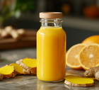 A small glass bottle filled with vibrant yellow ginger shot, surrounded by fresh ginger, turmeric roots, and sliced citrus fruits on a wooden surface