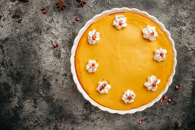 homemade pumpkin cheesecake with caramel sauce and seeds on top on metal wicker stand