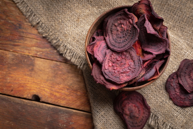 Beetroot chips in wooden bowl on burlap napkin on old wooden table.