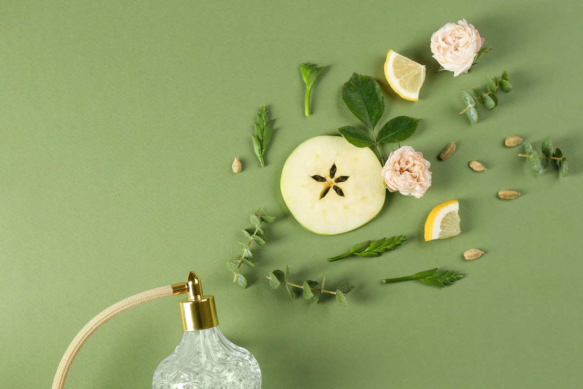 Flat lay composition with bottle of perfume on green background, space for text