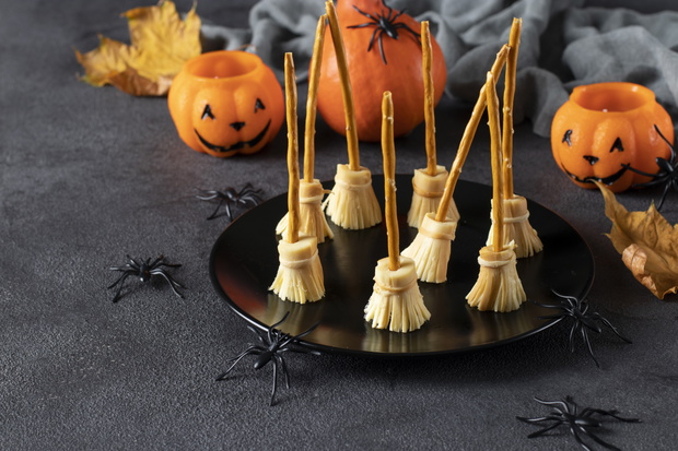 Witch broom made of cheese and bread straw for the celebration of Halloween on dark background