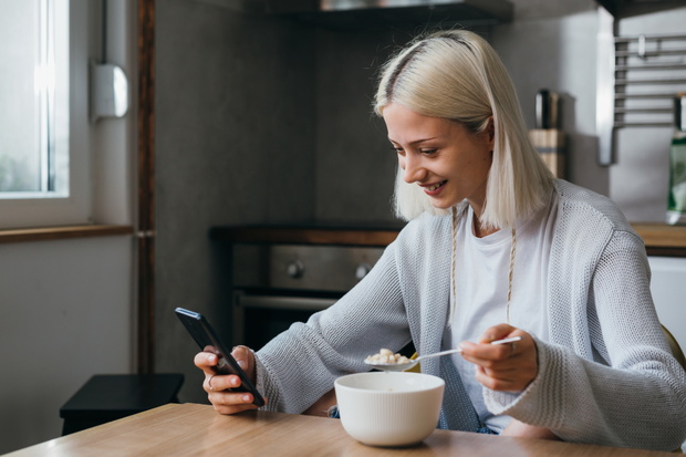 woman having breakfast at home and using mobile phone