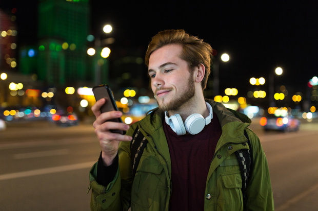 Young man using smartphone on urban street at night
